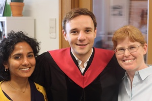 Two clinical instructors smile with a student who is wearing graduation robes.